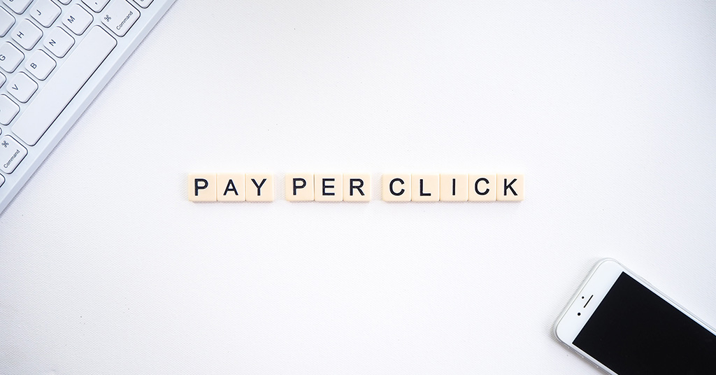 Pay per Click Spelled out in single tiles on white background with keyboard and iphone